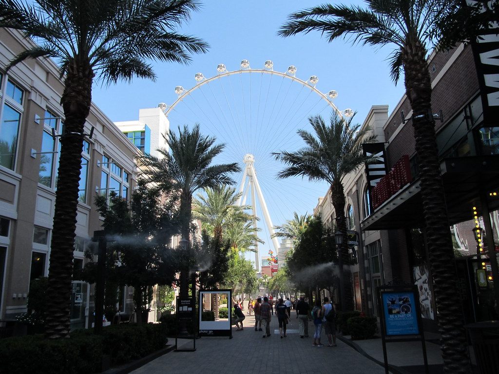 People strolling down the palm-lined LINQ Promenade toward the High Roller observation wheel on a sunny day