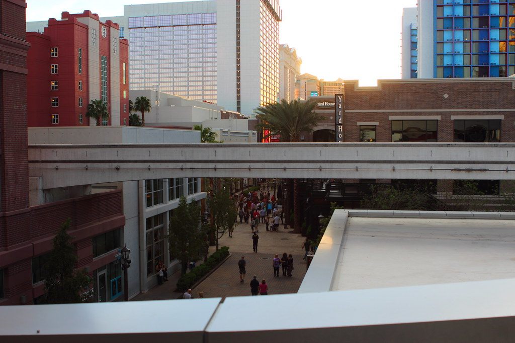 Evening crowds walking the LINQ Promenade seen from above, between brick-faced shops and the hotel towers of the center Strip