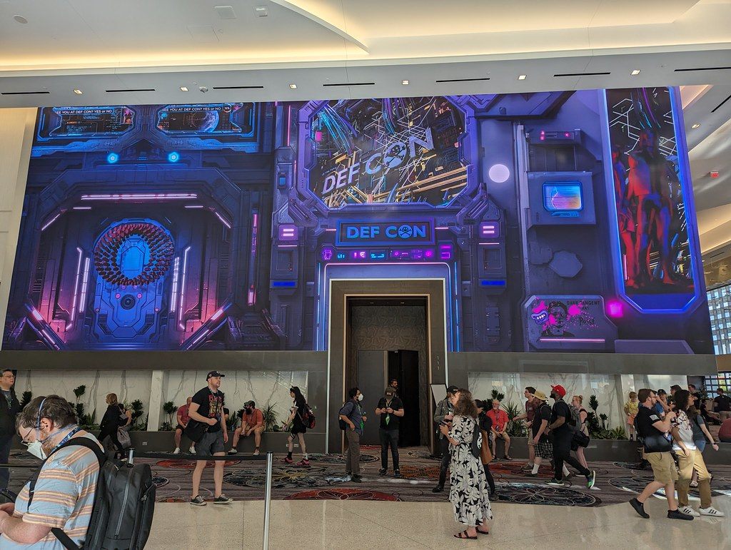 DEF CON 31 attendees in the Caesars Forum lobby in front of a floor-to-ceiling DEF CON video wall built around a doorway