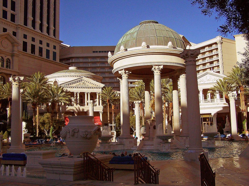Swimmers and loungers in the Garden of the Gods pool at Caesars Palace, framed by a domed rotunda and Roman columns