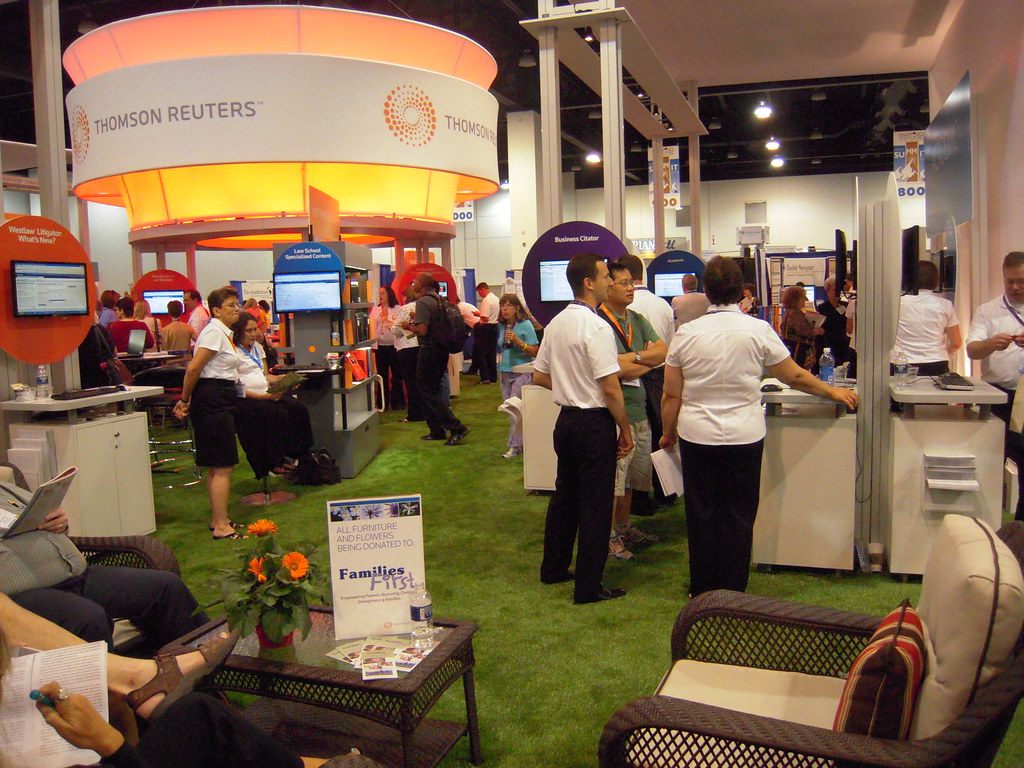 Exhibitors and attendees at a lounge-style booth with artificial turf and an orange ring sign on the AALL 2010 exhibit floor at the Colorado Convention Center