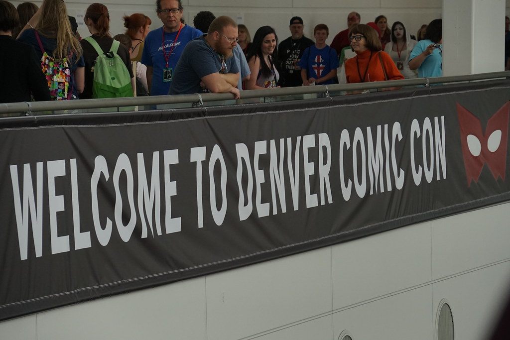 Fans lean on a rail above a Welcome to Denver Comic Con banner