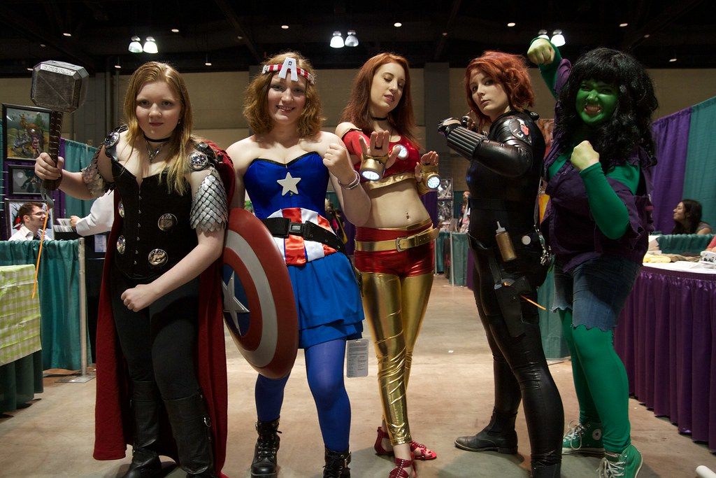 Five cosplayers in gender-swapped Avengers costumes posing between exhibitor booths at ConnectiCon 2012