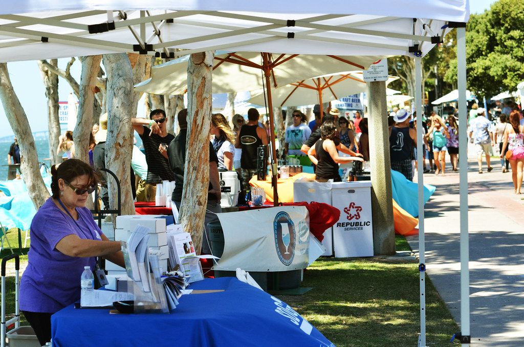 Visitors browsing exhibitor tents under trees along a bayside path at the 2014 Chula Vista HarborFest