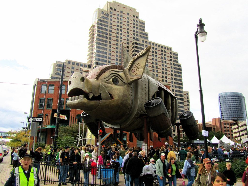 Crowds on a downtown Grand Rapids street beneath the giant Steam Pig sculpture during ArtPrize 2010, with the Amway Grand Plaza tower behind