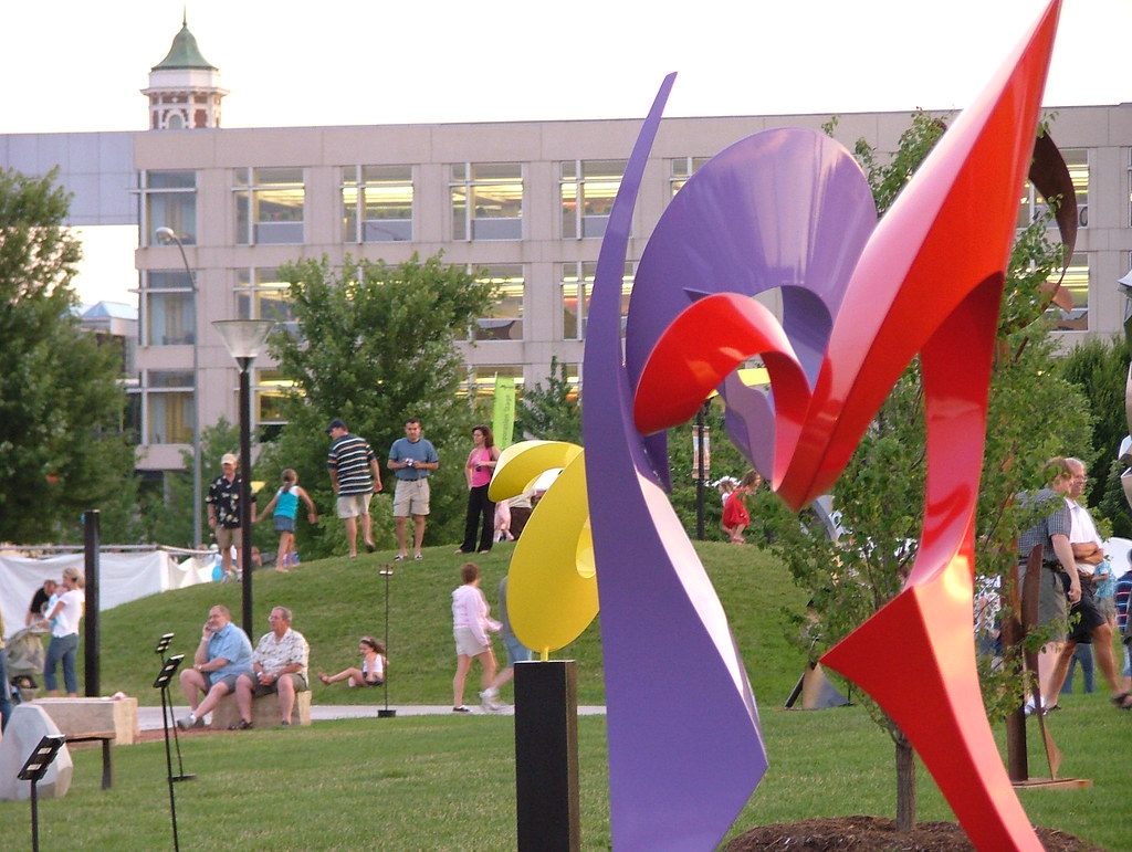 Visitors strolling past a large red, purple and yellow metal sculpture on a lawn during the Des Moines Arts Festival