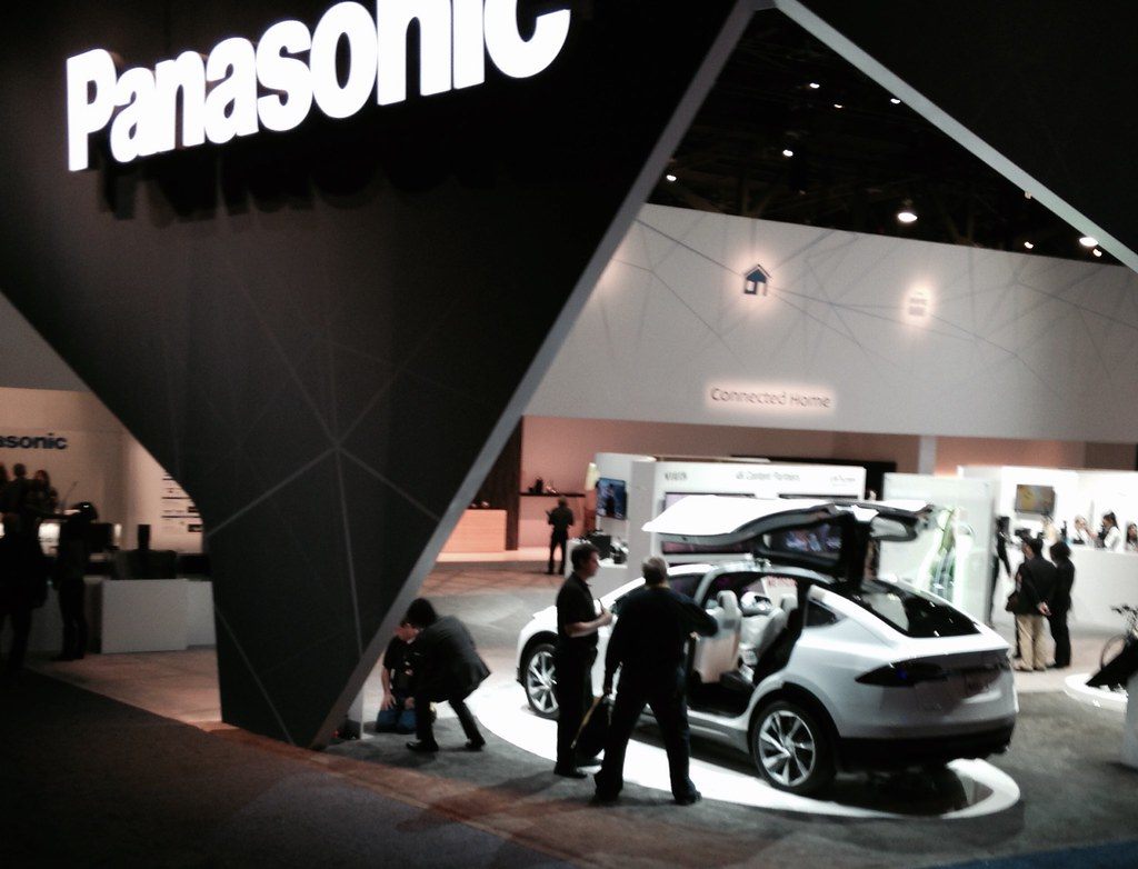 Visitors gathered around a white Tesla Model X with its falcon-wing doors open inside a Panasonic exhibit at CES