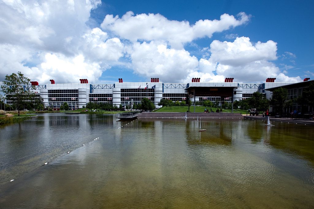 The long white George R. Brown Convention Center with its red stacks seen across the reflecting lake at Discovery Green under a big blue sky