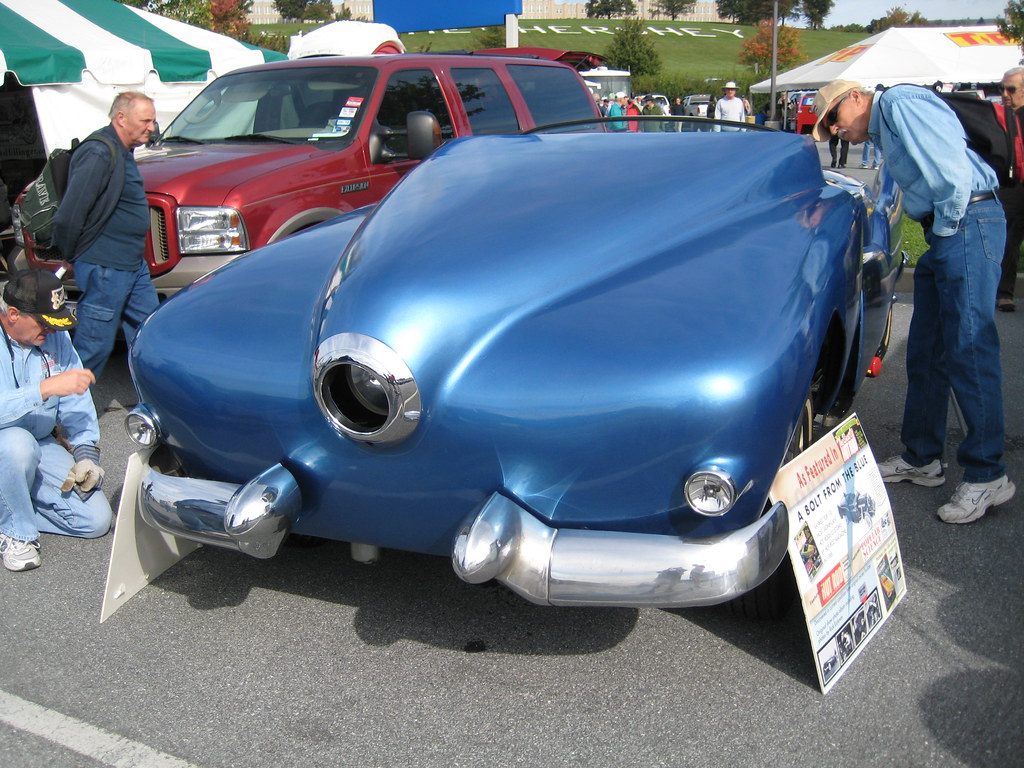 Visitors lean in to inspect a blue custom-bodied car in the swap-meet field at the AACA Hershey fall meet, with the HERSHEY hillside letters behind