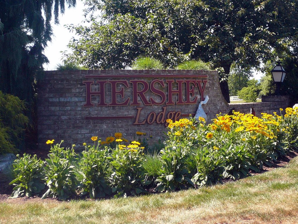 The brick Hershey Lodge entrance sign on University Drive, with yellow flowers planted in front