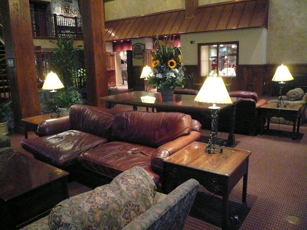 Leather sofas, table lamps and a flower arrangement under the timber beams and stone fireplace wall of a Hershey Lodge lobby lounge