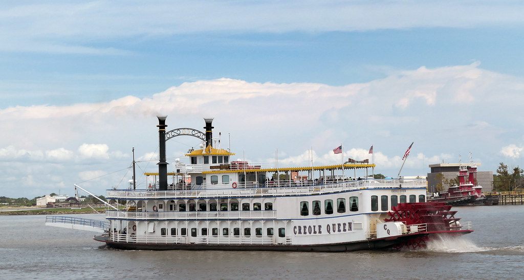 The white Creole Queen paddlewheeler with a red paddle wheel cruising on the Mississippi River