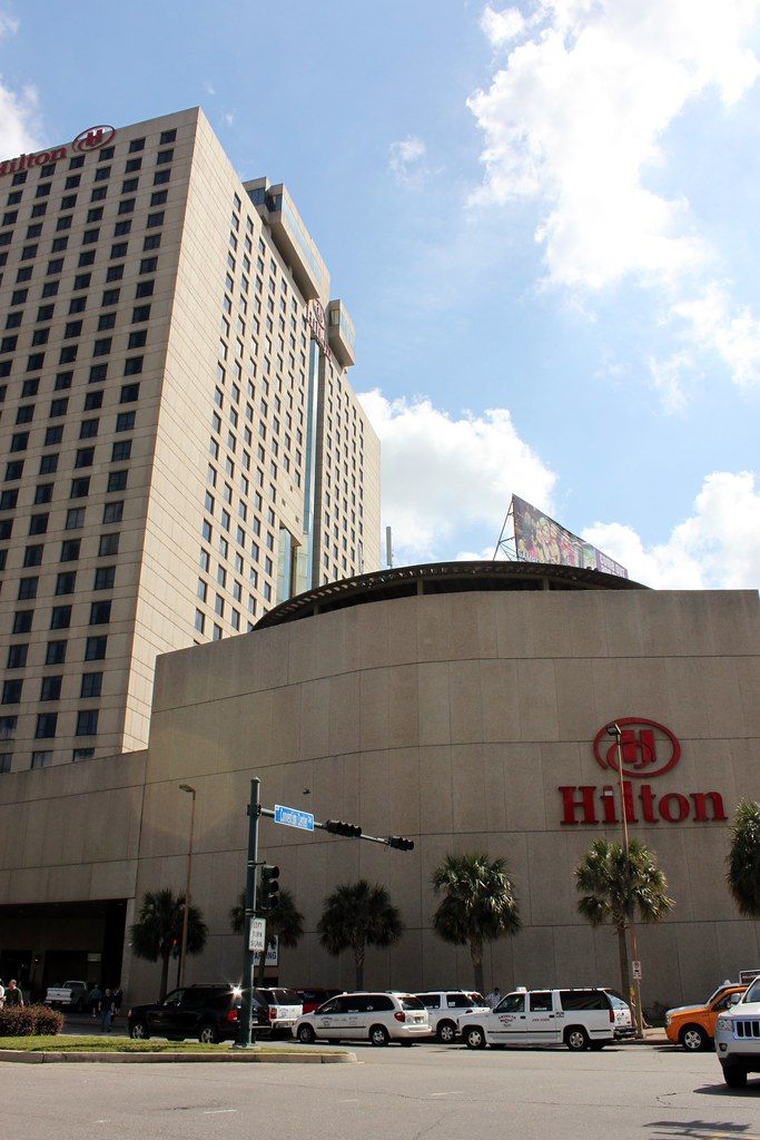 The Hilton New Orleans Riverside tower and its curved low-rise wing with a red Hilton sign, at a corner with a Convention Center Blvd street sign