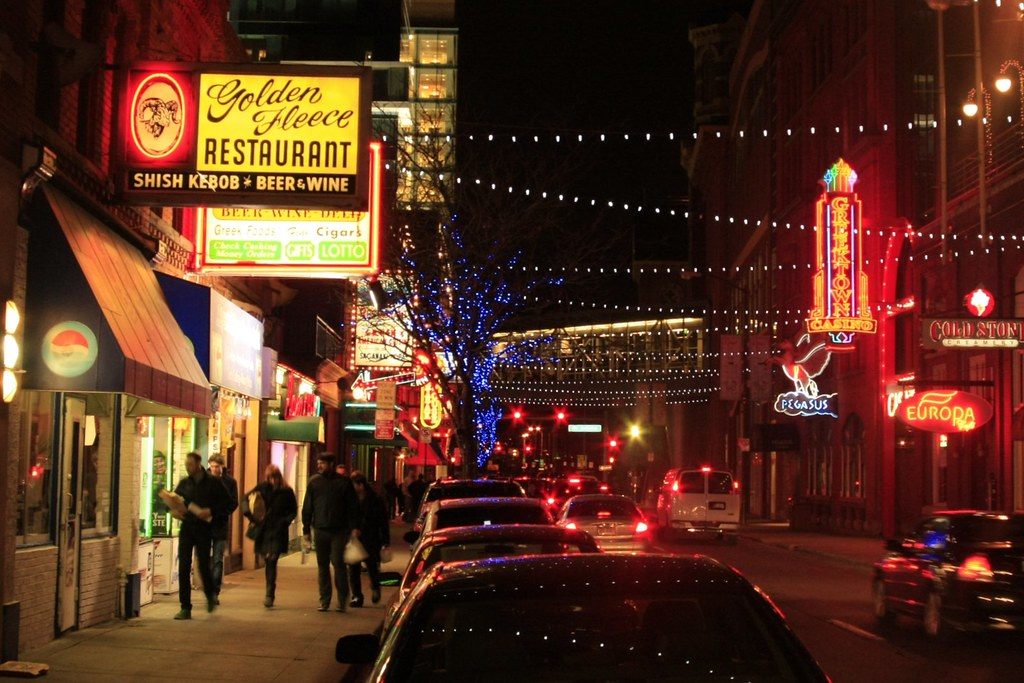 People walking under neon restaurant signs and strings of lights on Monroe Street in Detroit's Greektown on a Saturday night