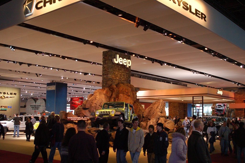 Show-goers walking past a Jeep Wrangler perched on a rock display under the Chrysler and Jeep stand canopy at the 2008 North American International Auto Show in Detroit