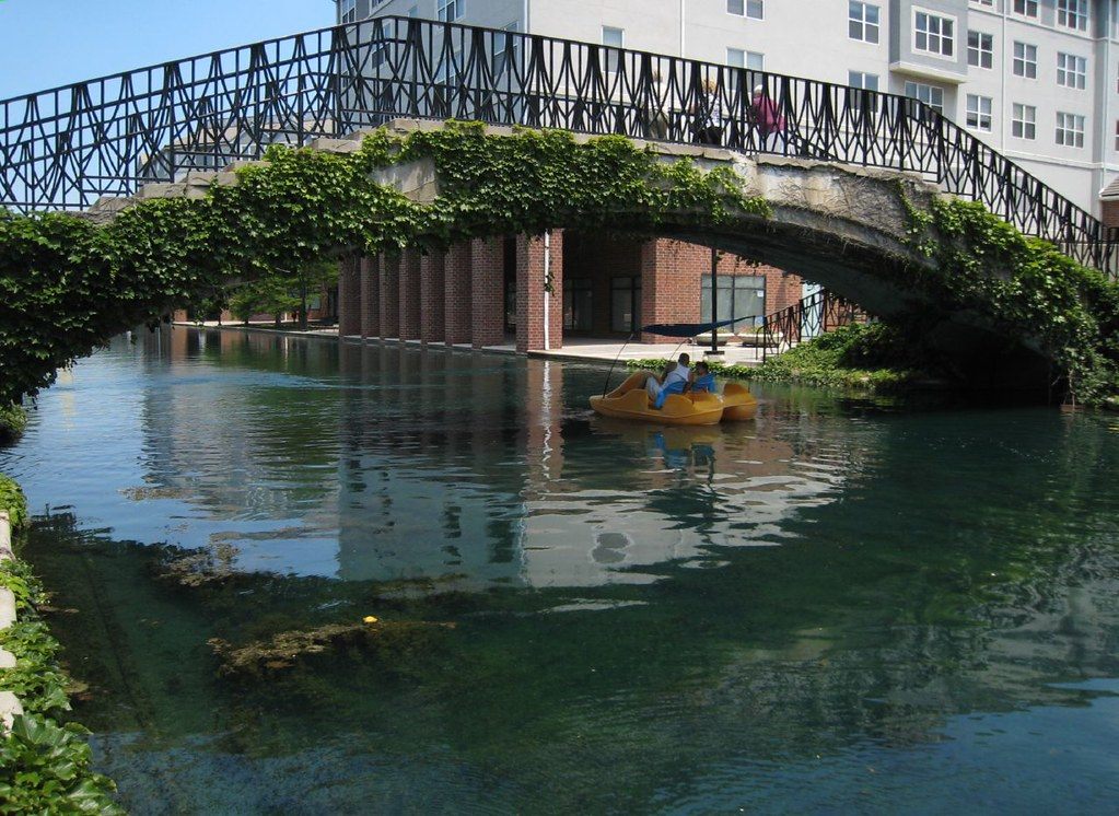 A yellow pedal boat glides under an ivy-covered stone bridge on the Indianapolis Canal