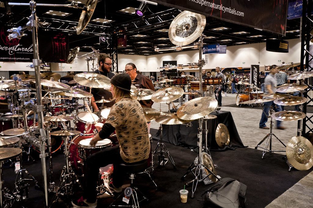An exhibitor plays a drum kit inside a booth hung with dozens of cymbals on the PASIC 2010 exhibit floor in Indianapolis