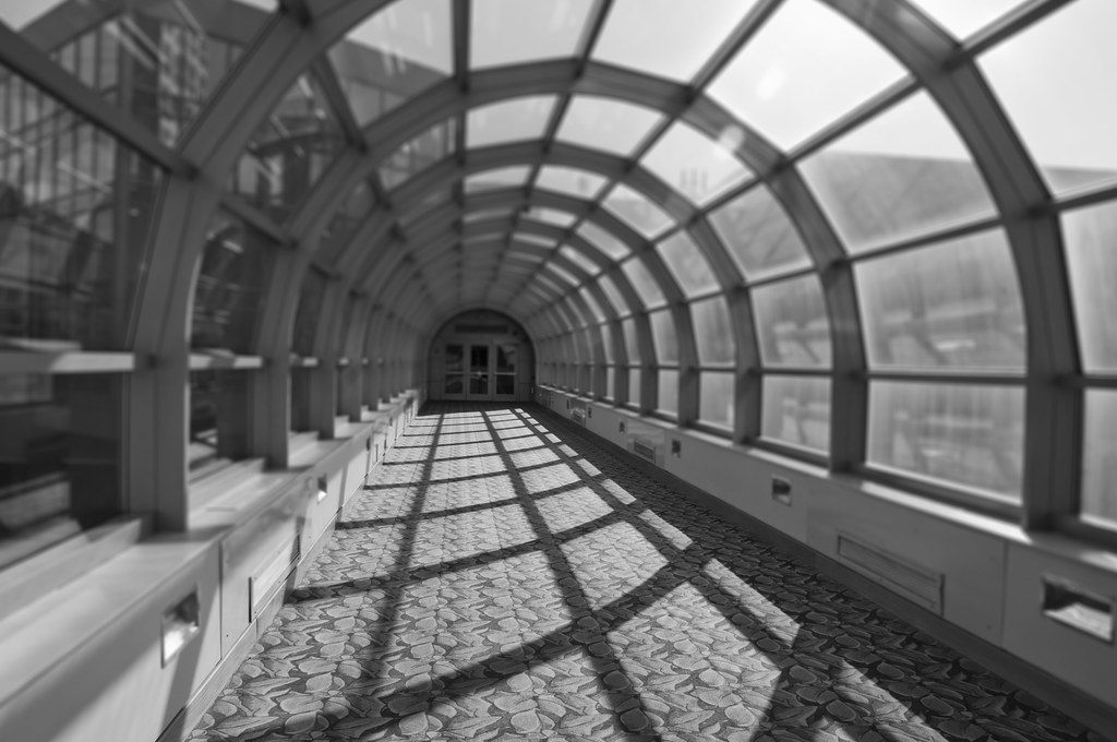 Black-and-white view down a glass-roofed skywalk with arched steel ribs leading to the Indiana Convention Center
