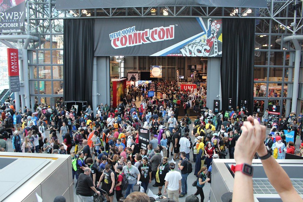 A packed crowd of New York Comic Con 2017 attendees, many in costume, filling the Javits Center Crystal Palace below a New York Comic Con banner