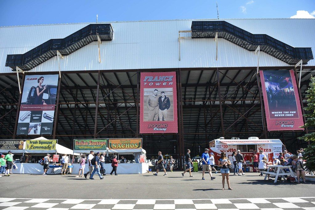 Race fans walking past lemonade and sausage stands below the France Tower grandstand banners at Pocono Raceway