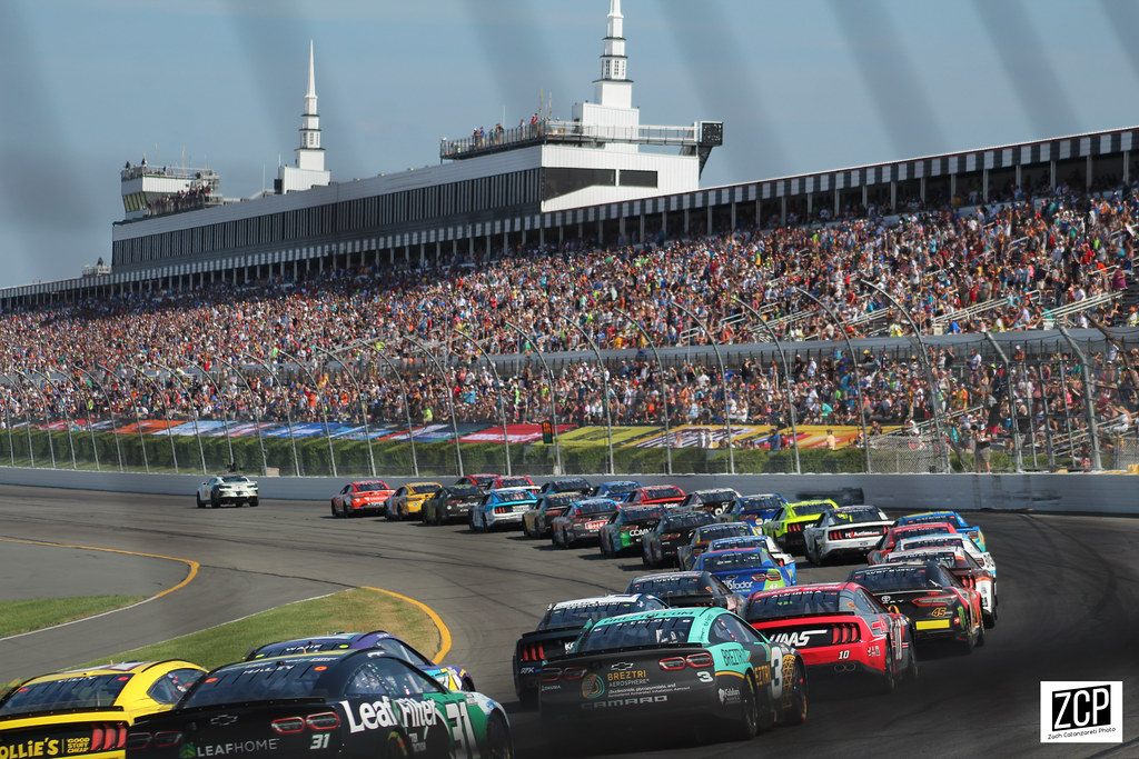 A packed grandstand watches a field of NASCAR stock cars take a restart at Pocono Raceway in Long Pond, Monroe County
