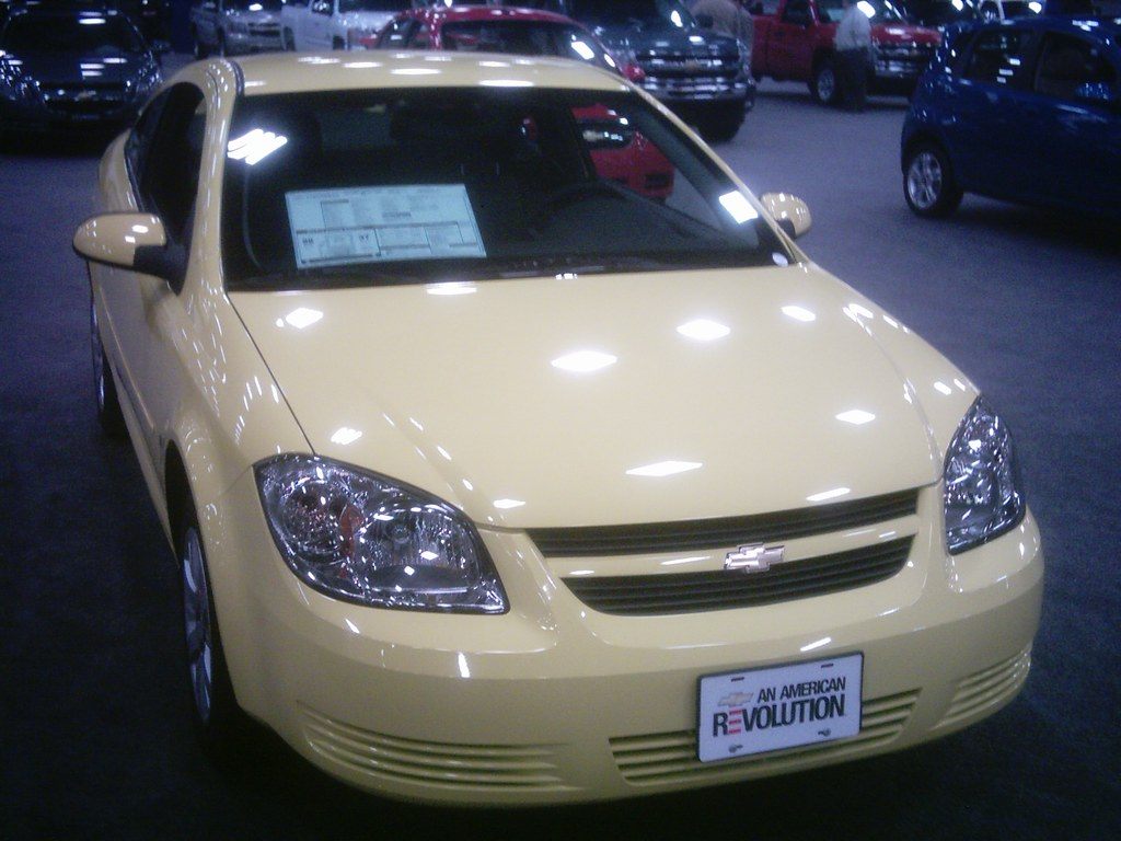 A pale yellow Chevy Cobalt on the carpeted floor at the 2009 Dallas Auto Show, with more cars behind