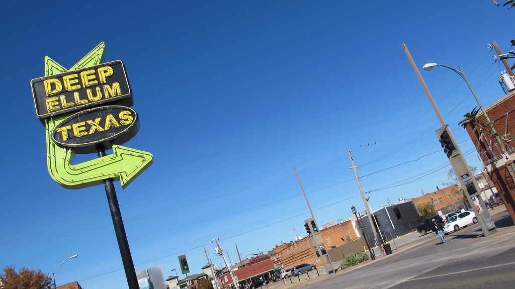 The neon arrow sign reading Deep Ellum Texas above a street corner in the Deep Ellum district of Dallas