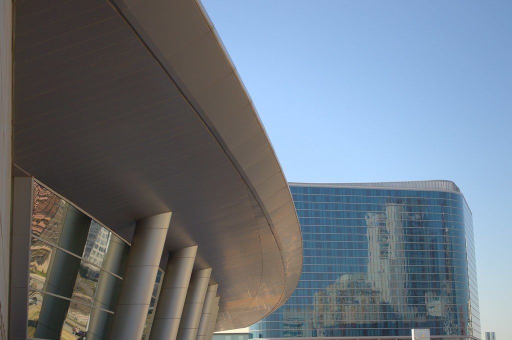 The curved white canopy and columns of the Dallas convention center sweeping toward the blue glass tower of the Omni Dallas Hotel