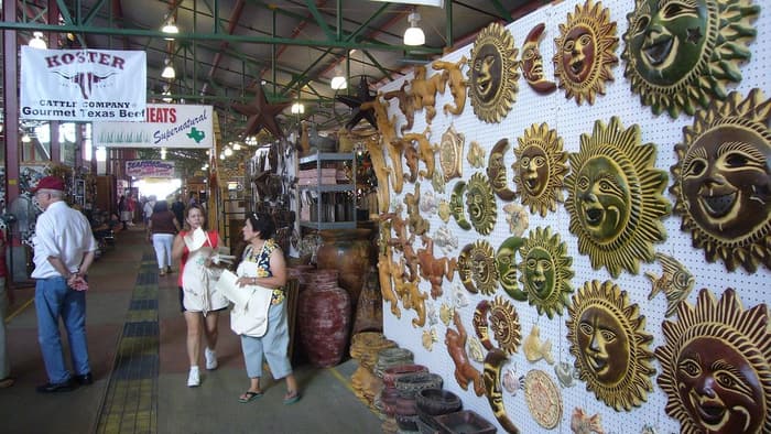 Shoppers walk past a wall of painted sun plaques and stalls inside a shed at the Dallas Farmers Market