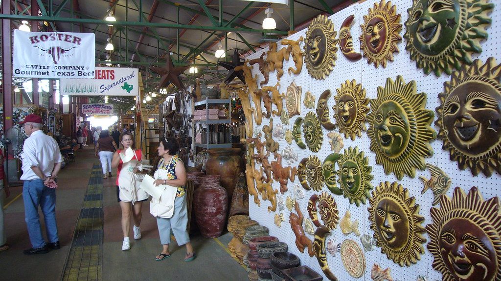 Shoppers walk past a wall of painted sun plaques and stalls inside a shed at the Dallas Farmers Market