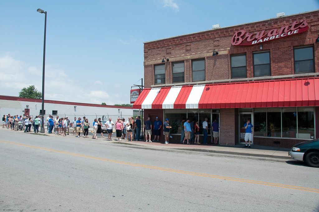 A long line of people on the sidewalk waiting outside Arthur Bryant's Barbecue under its red and white awning