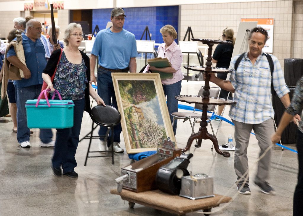 Visitors pushing carts and carrying paintings, furniture and a cooler through the Bartle Hall exhibit floor during the Antiques Roadshow taping