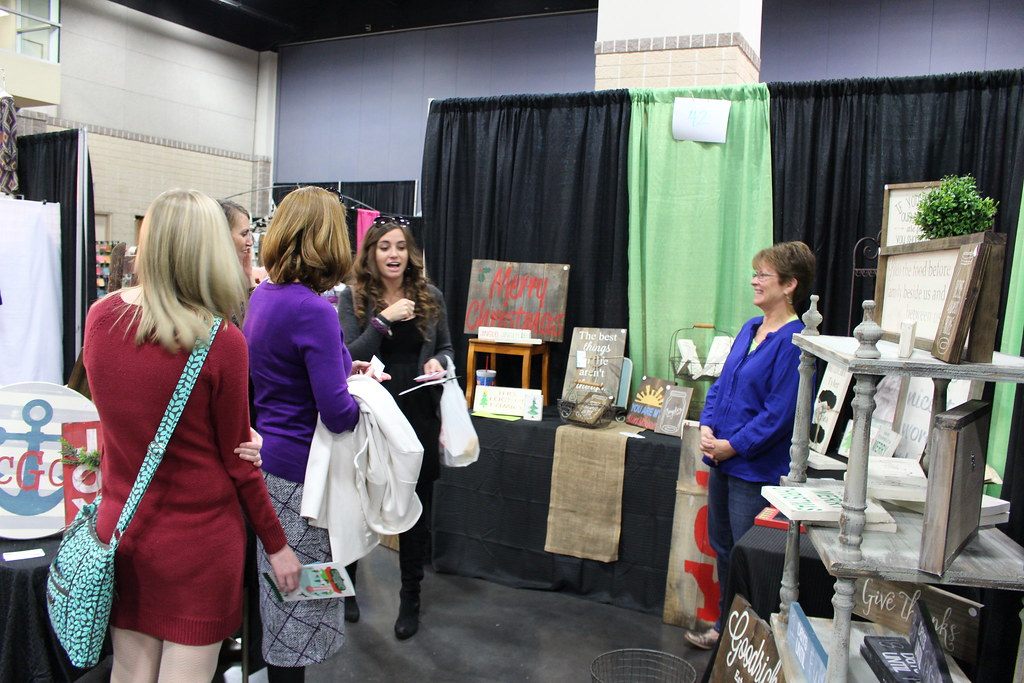 A vendor greets shoppers at a pipe-and-drape booth of hand-painted holiday signs during Tinsel and Treasure 2014 in Knoxville