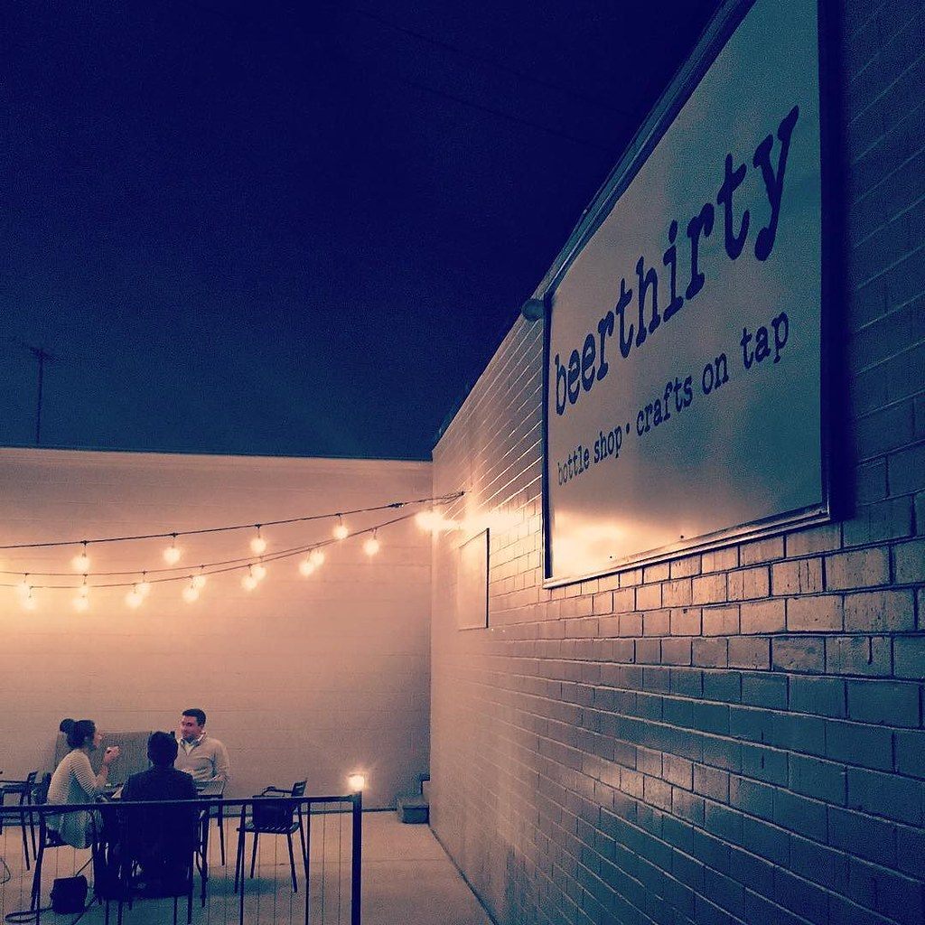 Friends at a table on the string-lit patio of the beerthirty bottle shop in downtown Greensboro at night