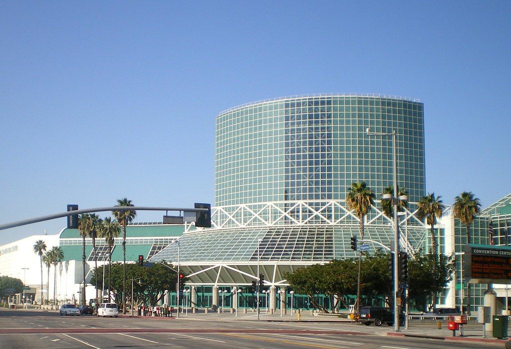 The green-glass tower and glass entrance pavilion of the Los Angeles Convention Center behind palm trees on a clear day