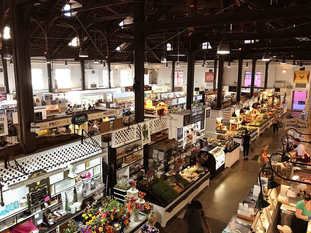 Shoppers browsing produce, flower and bakery stands beneath the timber roof of Lancaster Central Market