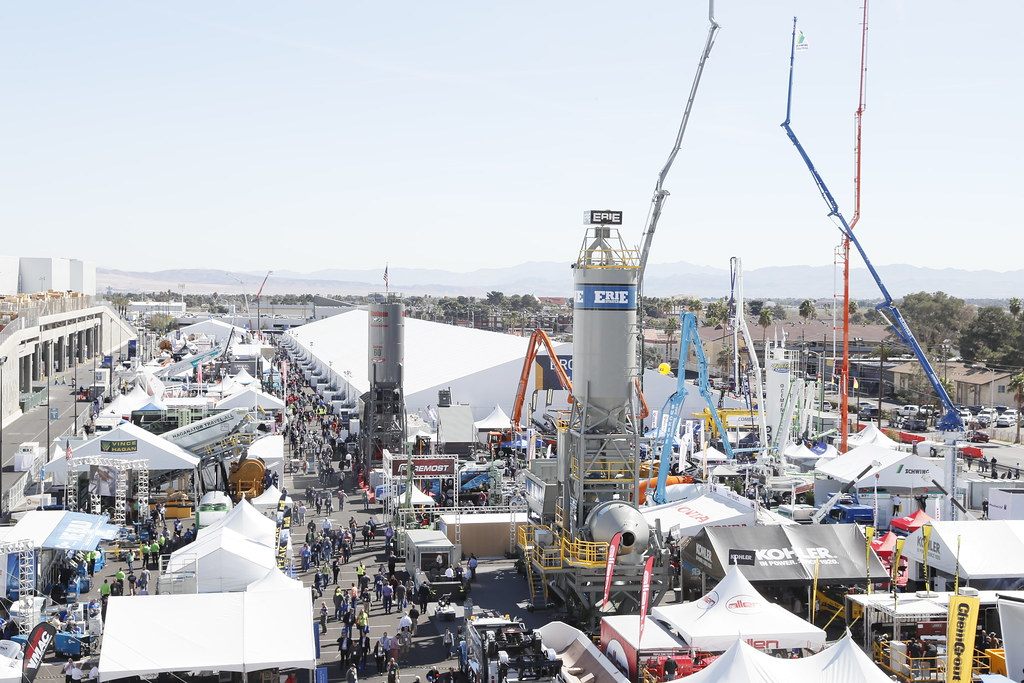 Aerial view of the outdoor CONEXPO-CON/AGG exhibit lots at the Las Vegas Convention Center, packed with white tents, a concrete plant tower and tall cranes, with mountains on the horizon