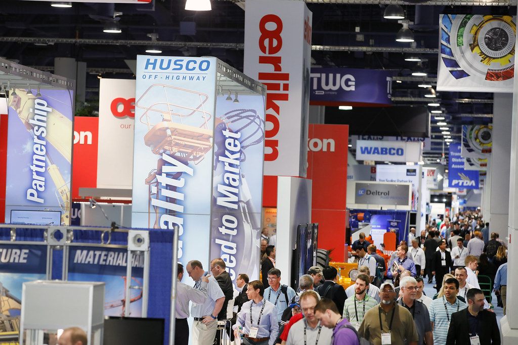 Attendees with lanyards crowding a long aisle of tall branded booth towers at IFPE 2017 in the Las Vegas Convention Center