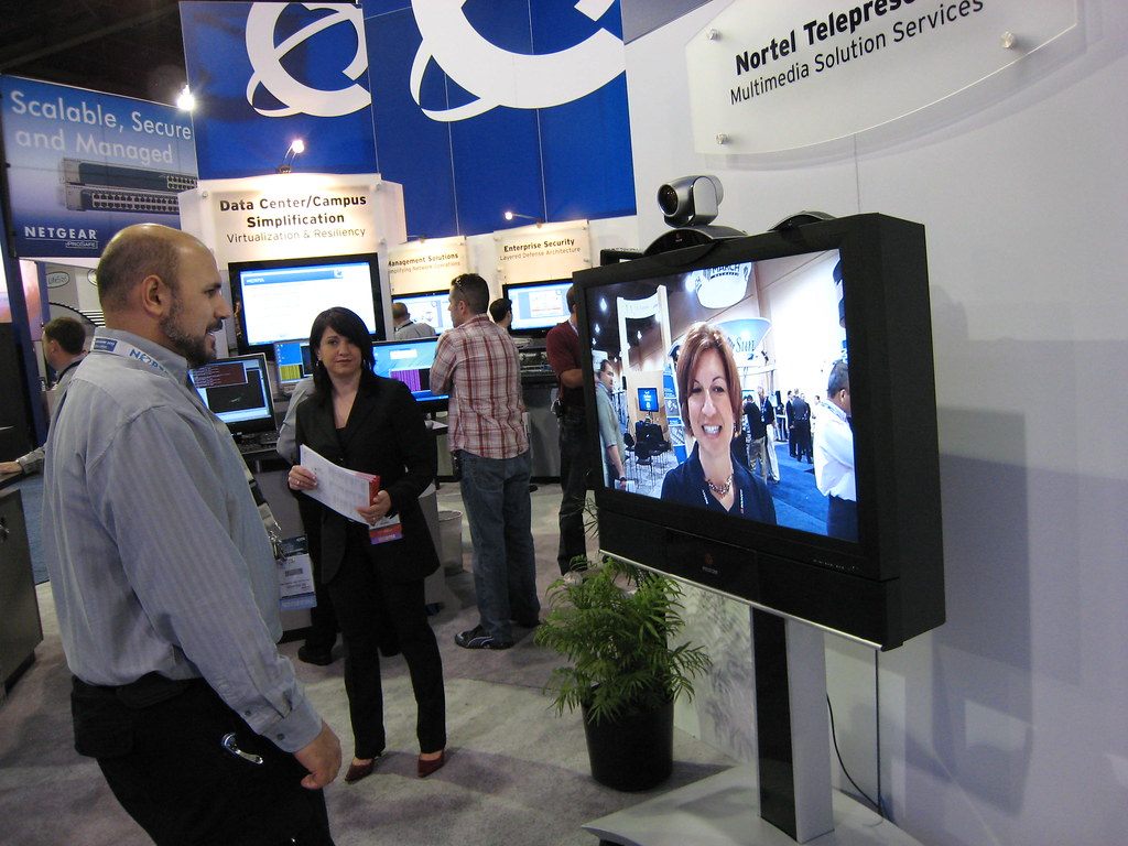 Visitors watching a telepresence video demo at a Nortel booth on the Interop Las Vegas 2008 show floor, with Netgear booth signs behind