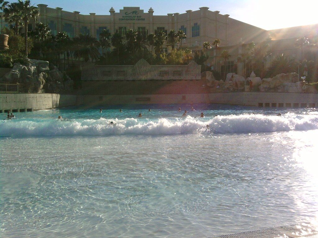 Swimmers in the wave pool at Mandalay Bay Beach with the Mandalay Bay Convention Center sign on the building behind the palms