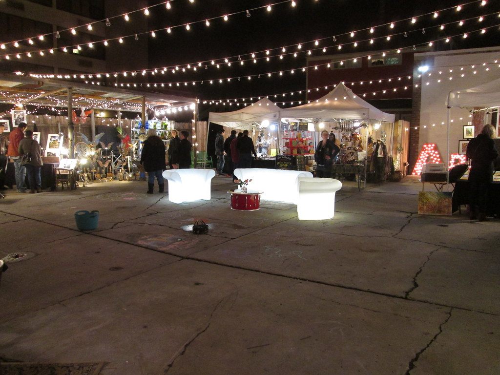 Shoppers browse lit tents under strings of lights at the Frenchmen Art Market at night