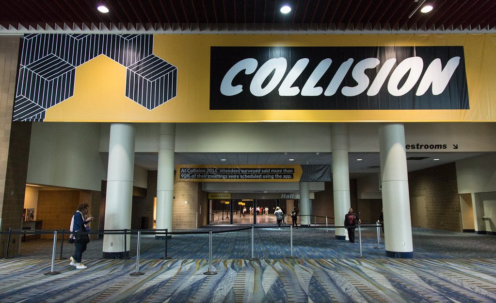 A yellow Collision banner over a wide carpeted entrance hall with tall white columns
