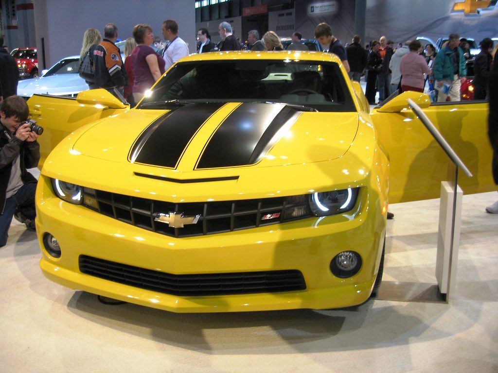 A crowd around a yellow Chevrolet Camaro with black stripes and open doors at the 2010 Chicago Auto Show