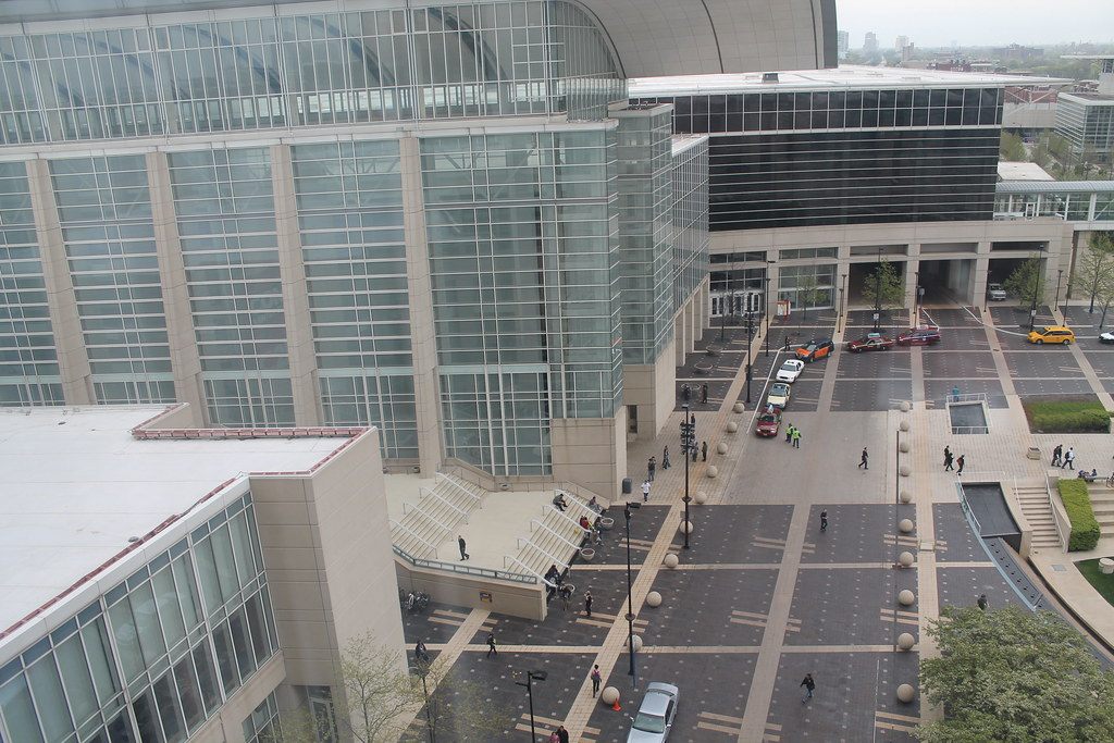 Glass curtain walls of McCormick Place buildings around a paved plaza and drop-off drive, seen from above