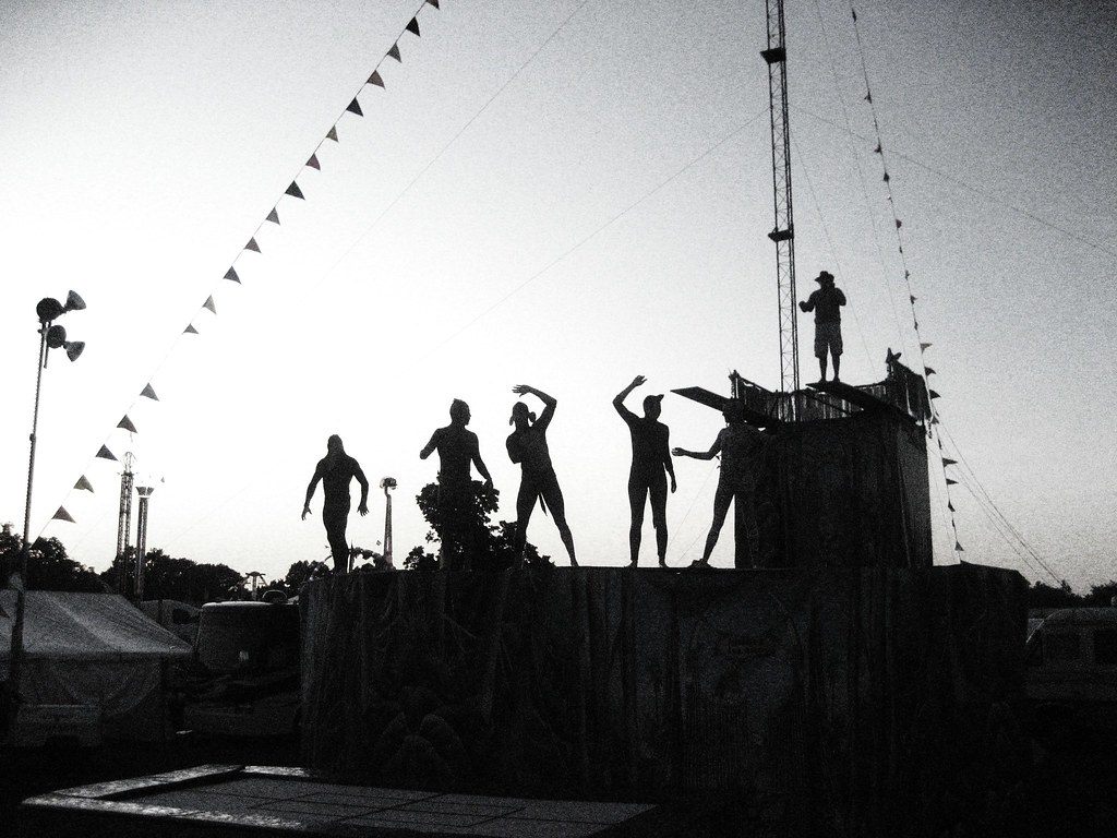 Silhouetted figures pose on a fairground stage under pennant flags and a light tower at dusk at the Dutchess County Fair in Rhinebeck, NY