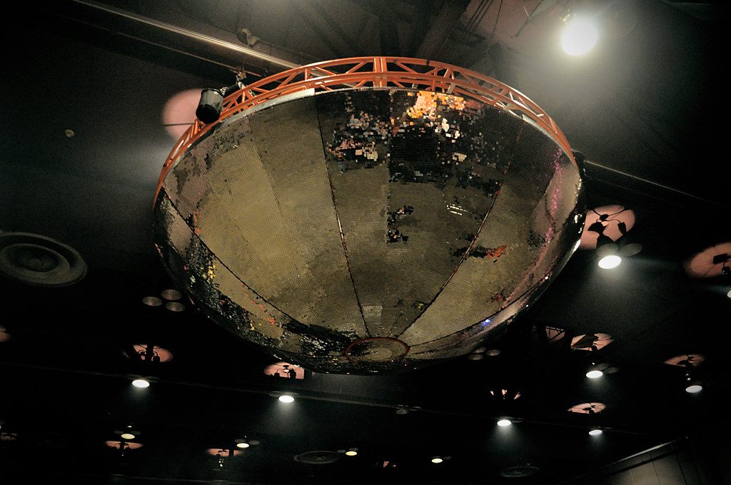A mirrored half-dome stage prop hanging from an orange truss under the ceiling lights of the Mid-Hudson Civic Center during a 2010 concert