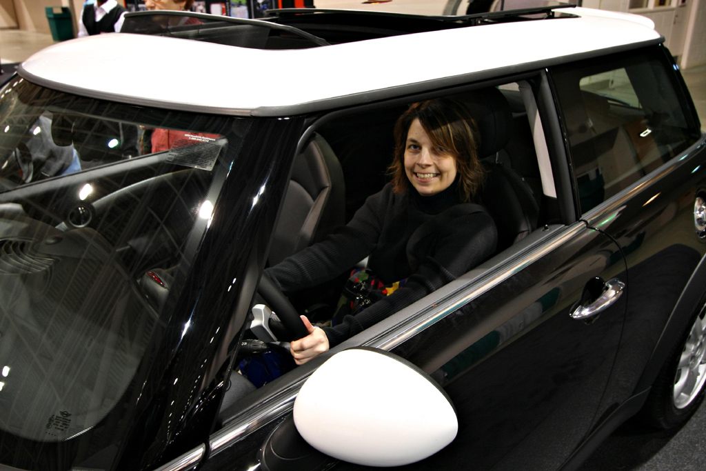 A smiling visitor sitting behind the wheel of a black MINI with a white roof at the 2010 Twin Cities Auto Show