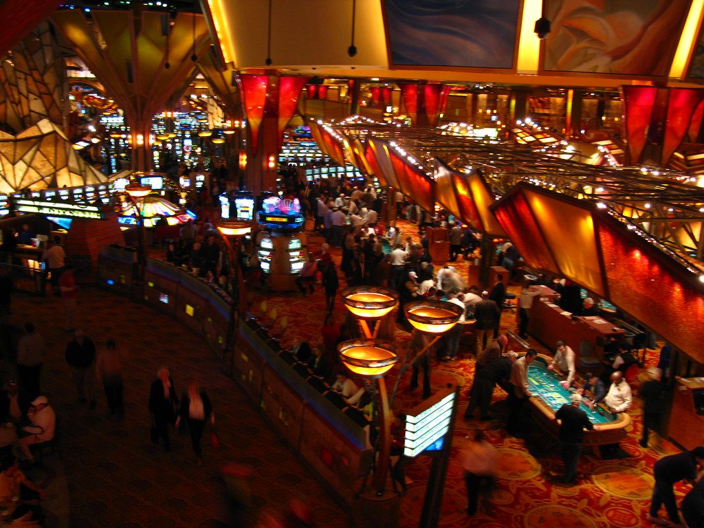 Players and visitors crowd the gaming tables and walkways under the glowing canopy of the casino floor at Mohegan Sun, Uncasville