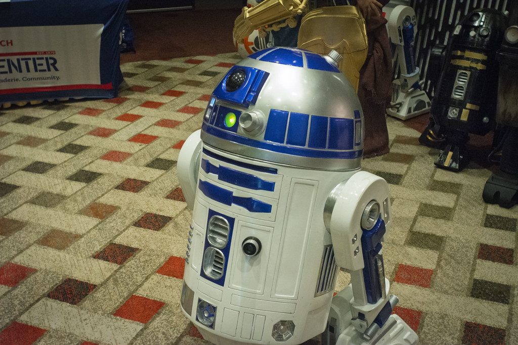A fan-built R2-D2 droid on the patterned expo carpet, with more fan-built droids behind it, at Terrificon 2024