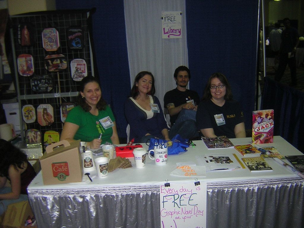 Smiling exhibitors behind a skirted table promoting free graphic novels for libraries at the 2008 Pittsburgh Comicon